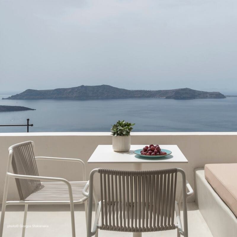 Two white Tribeca Stoneli chairs with woven rope seat and back, positioned on a balcony overlooking the sea and islands in the background. 