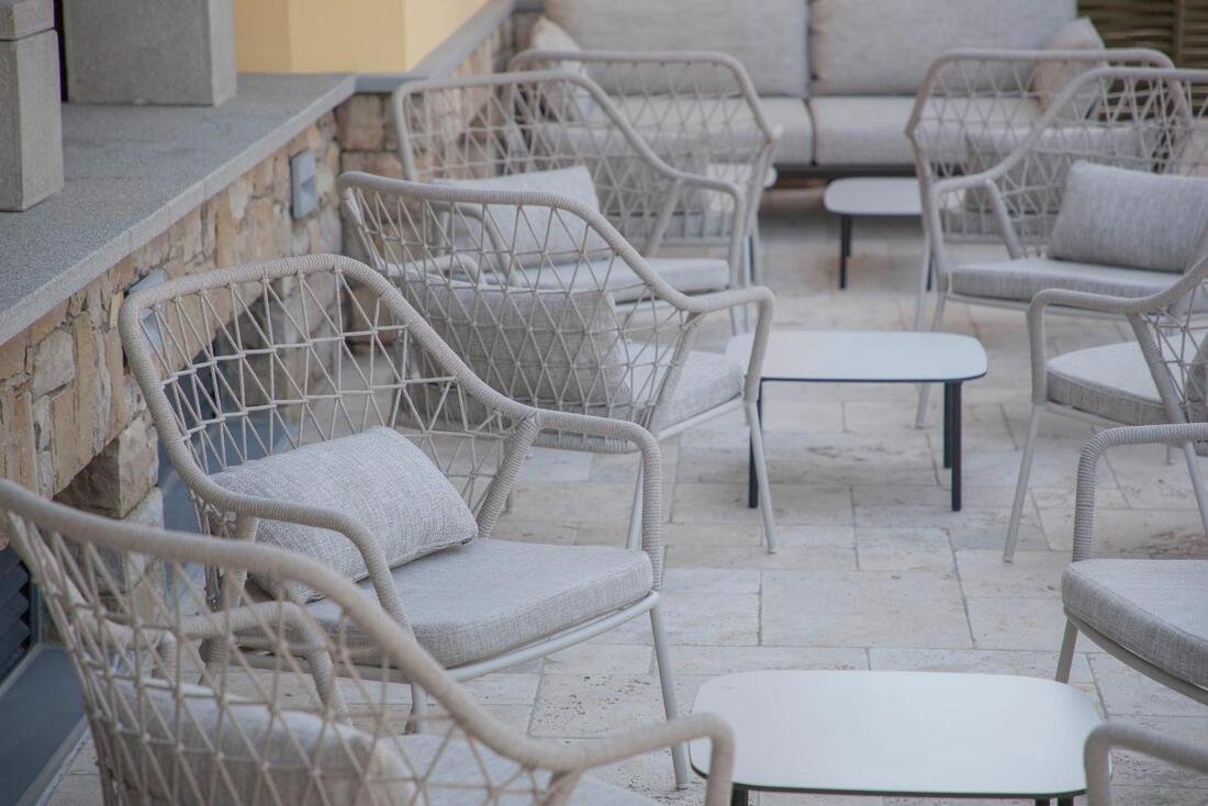 Set of Pedrali Panarea outdoor armchairs and chairs with white frame and beige woven rope, arranged around low tables on a modern terrace. 