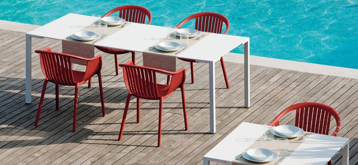 Four red polypropylene chairs, Pedrali Tatami Outdoor Chair 306, arranged around white tables next to a swimming pool.