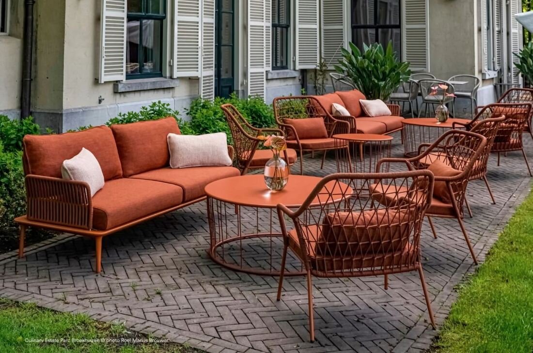 Pedrali Reva terracotta lounge sofas with Pedrali Panarea 3675 chairs and round woven rope coffee tables in an outdoor dining space. 