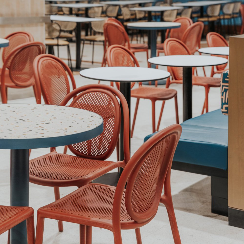 bar with Pedrali Remind chairs in terracotta red polypropylene with perforated oval backrest, arranged on round tables in a cafeteria environment