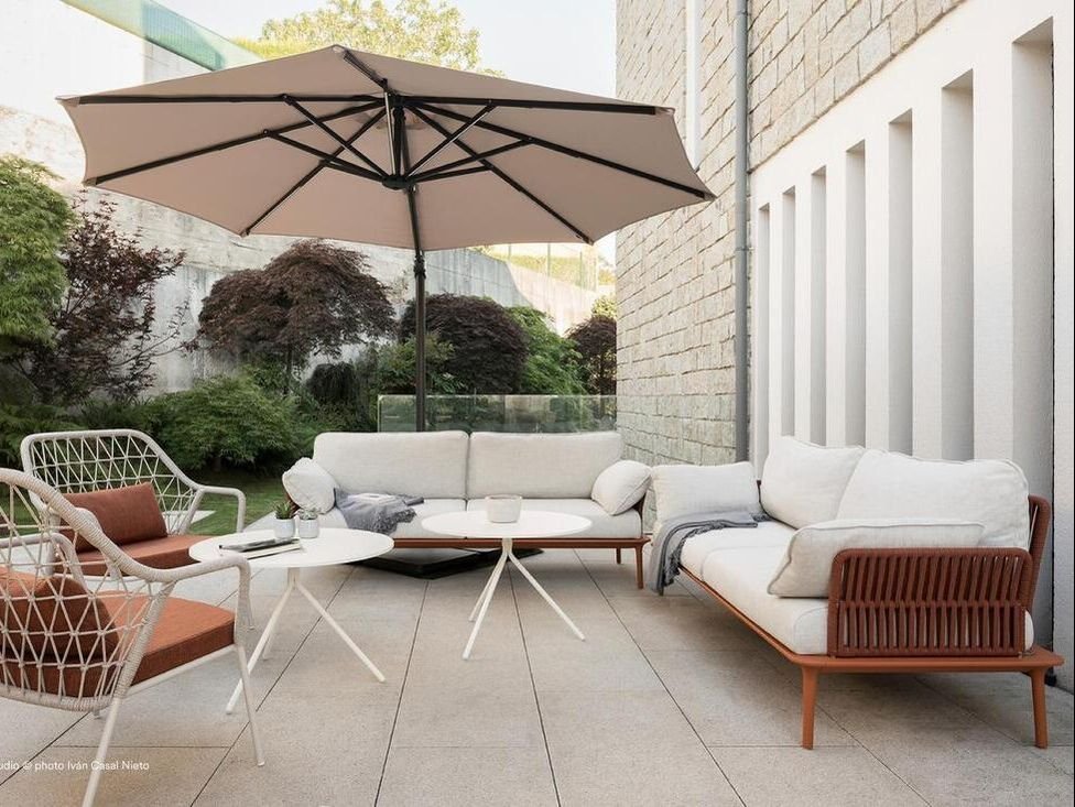 White Pedrali Reva sofa and armchair with cushions and umbrella on a hotel terrace. 