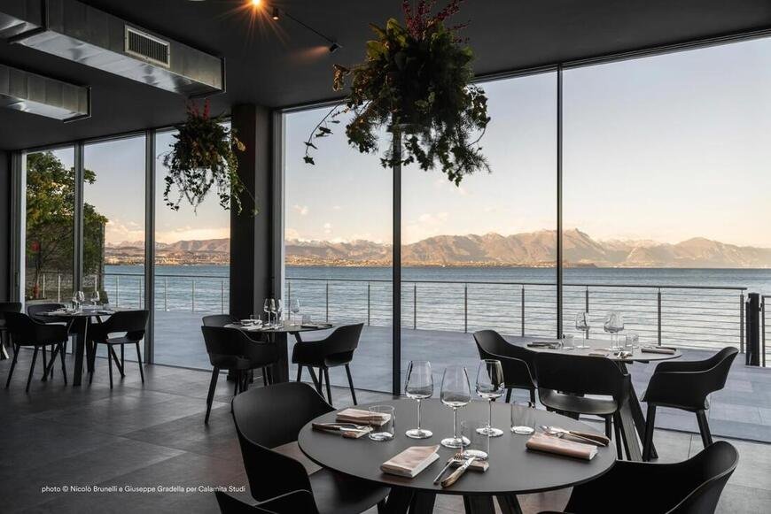 Pedrali Elliot round tables with black chairs in a modern restaurant with panoramic lake and mountain views. 