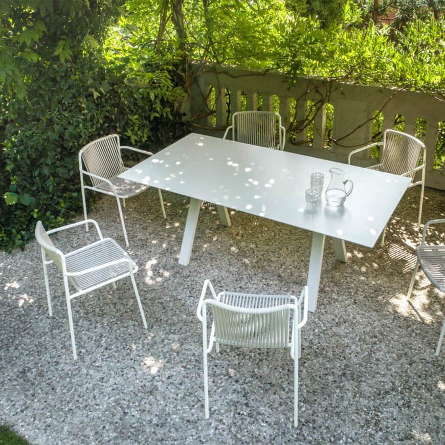 Set of six white Pedrali Tribeca 3665 chairs with woven rope seat and back, arranged around a white rectangular table in a gravel garden. 